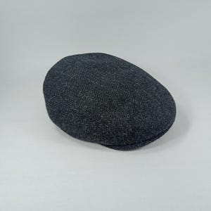May include: A dark gray tweed flat cap with a herringbone pattern. The cap has a rounded crown and a small, stiff brim. The fabric appears to be a woven wool blend. This classic style hat is suitable for various occasions.