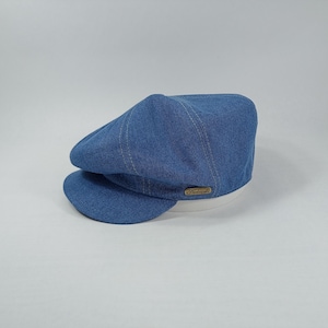 May include: A blue denim newsboy cap with a white brim and a brown leather label that says "Handwoven".