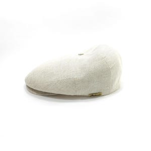 May include: A light beige newsboy cap made of linen fabric. The cap has a rounded crown, a small brim, and a small button on top. A small, rectangular tag is sewn on the side.