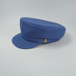Op de afbeelding: Een blauwe linnen pet met een knoop bovenop. De pet heeft een brede rand en een platte kroon.