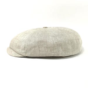 Peut inclure: Casquette de style gavroche beige clair, fabriquée dans un tissu texturé. Elle présente une couronne arrondie et une petite visière incurvée. La couleur neutre suggère une matière respirante, adaptée aux températures plus chaudes. Un accessoire de mode classique.