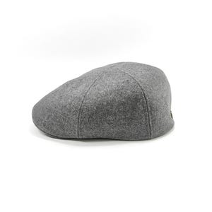 Könnte beinhalten: Graue Flatcap aus weichem Stoff. Die Mütze hat eine runde Krone und einen kleinen, steifen Schirm. Die Kappe ist einfarbig und für Freizeitkleidung geeignet.