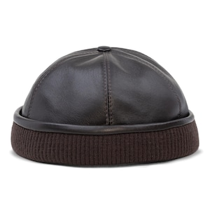 May include: A dark brown leather cap with a ribbed, dark brown knit brim. The cap has a rounded crown and a small, circular button at the top. The brim is a darker shade of brown than the crown.