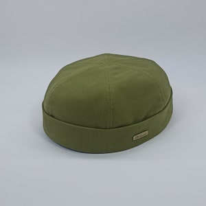 May include: A green cotton newsboy cap with a brown leather label that says "Remarkable".
