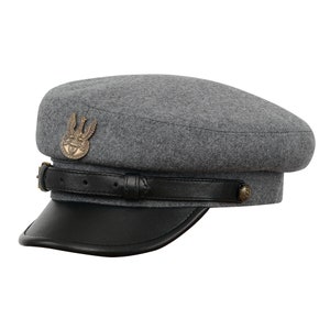 以下が含まれることがあります： グレーのウール素材のキャップで、黒い革のつばと金の鷲のエンブレムが付いています。