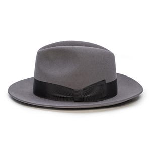 May include: A grey fedora hat featuring a black ribbon band and bow. The hat has a traditional, structured design with a wide brim. This hat is a versatile accessory, suitable for various occasions.