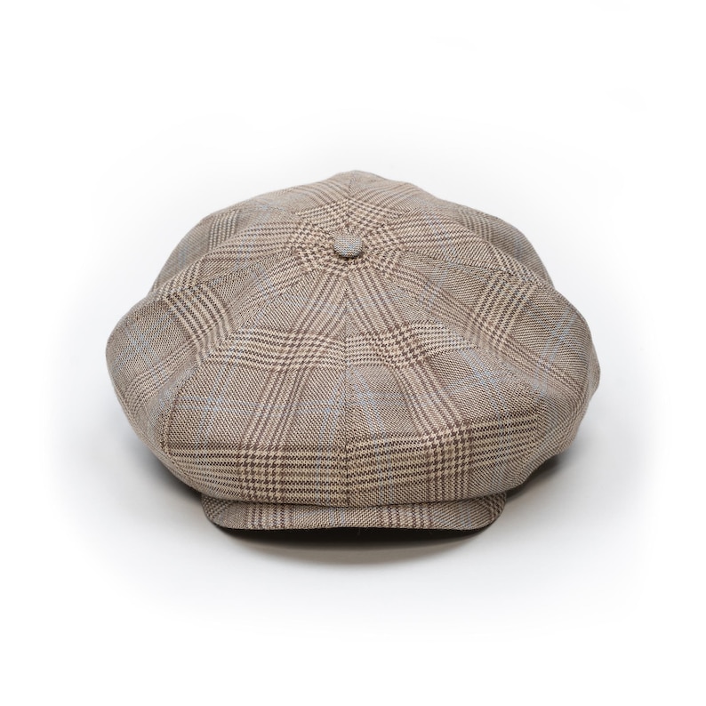 Pu&ograve; includere: Un cappello newsboy a quadri marrone e beige con corona arrotondata e piccola visiera rigida. Il cappello presenta un bottone sulla parte superiore e un design classico e su misura. Il tessuto ha un aspetto sottilmente strutturato.