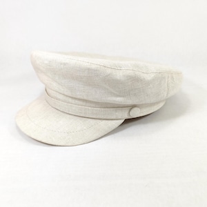 May include: A light beige linen baker boy hat with a rounded crown and a short, stiff brim. The hat features a band around the crown and a small button detail. The hat is a neutral color and is suitable for various outfits.