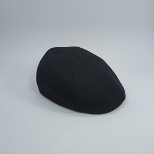 以下が含まれることがあります： 丸いクラウンとわずかに湾曲したつばを持つ、黒いウール製のフラットキャップです。