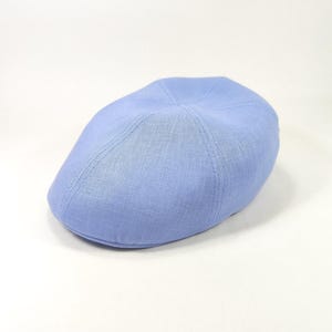 Pode incluir: Boné azul claro. O boné é feito de um tecido texturizado e apresenta uma coroa arredondada e uma aba curta e rígida. O boné é de cor sólida e parece novo.