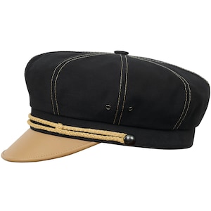 Peut inclure: Une casquette de marin en toile noire et cuir avec une bordure en corde dorée et un bouton noir.