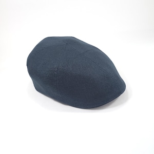 Peut inclure: Casquette gavroche bleu marine, avec une couronne arrondie et une courte visière rigide. La casquette est faite d'un tissu texturé et est posée sur un fond blanc. Ce chapeau classique est adapté à diverses occasions.