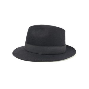Può includere: Un cappello fedora nero con un nastro di gros-grain. Il cappello ha una forma classica e strutturata con una tesa larga e una corona leggermente incavata. Il cappello è realizzato in un materiale morbido simile al feltro.