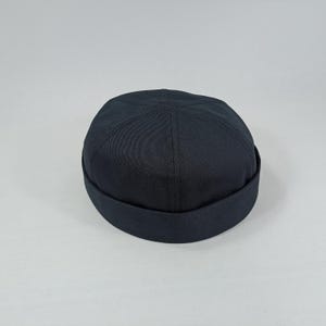 May include: A black cotton cap with a rounded crown and a flat brim. The cap has a simple design and is made of a soft, comfortable fabric.