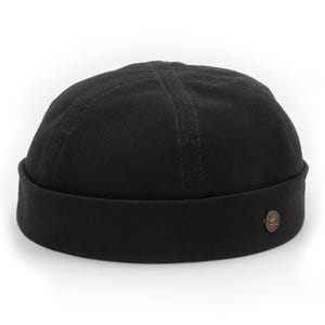 May include: A black skull cap with a rolled brim and a small, circular bronze-colored button on the side. The cap has visible stitching details on the crown. The hat is made of a sturdy fabric and is suitable for various casual outfits.