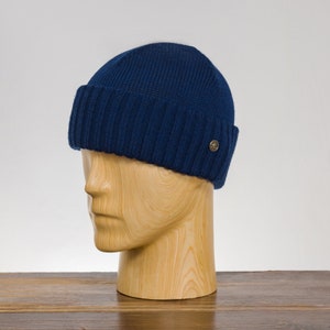 May include: A navy blue knitted beanie with a ribbed brim and a small gold logo on the side.