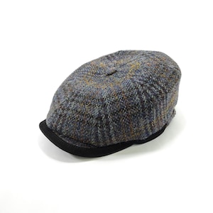 May include: A tweed newsboy cap in shades of grey, blue, and yellow. The cap has a rounded crown and a short, black brim. The fabric has a textured appearance.