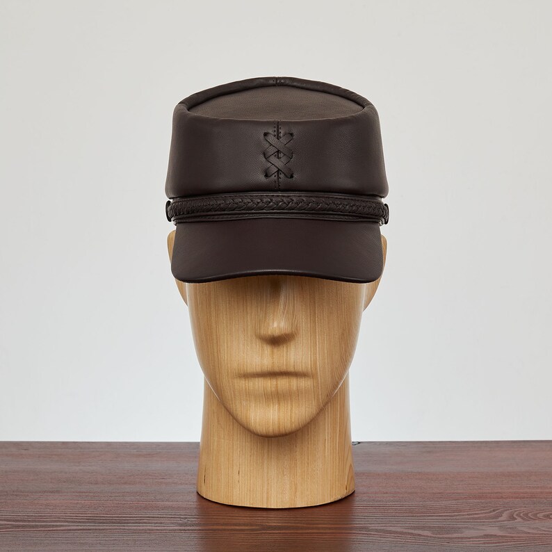 May include: A brown leather cap with a braided band and a stitched X design on the crown.