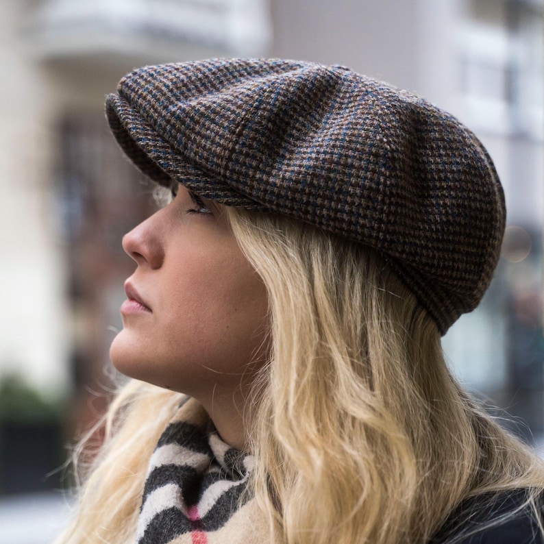 Puede incluir: Una mujer con una gorra de estilo newsboy de color marr&oacute;n y azul con una visera marr&oacute;n. La gorra est&aacute; hecha de tejido de tweed y tiene una corona ligeramente redondeada.