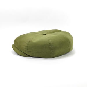 May include: Olive green newsboy cap with a rounded crown and a small, stiff brim. The cap is made of a solid-colored fabric and features stitched detailing. This classic style is suitable for various casual outfits.