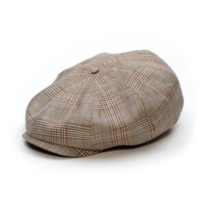 Pu&ograve; includere: Un berretto newsboy a quadri marrone e beige con una corona arrotondata e una visiera corta e rigida. Il berretto presenta un bottone sulla parte superiore e un design classico. Realizzato in tessuto.