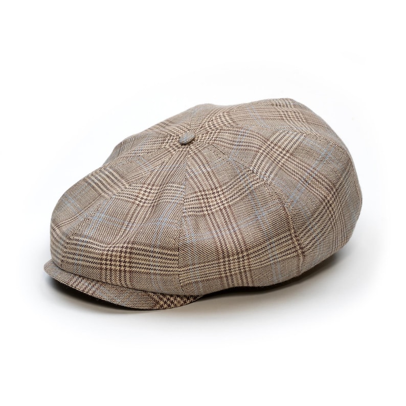 Pu&ograve; includere: Un berretto newsboy a quadri marrone e beige con una corona arrotondata e una visiera corta e rigida. Il berretto presenta un bottone sulla parte superiore e un design classico. Realizzato in tessuto.