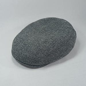 May include: A gray, textured flat cap. The hat has a rounded crown and a small, stiff brim. The fabric appears to be a woven material, and the cap is a solid, neutral color. This classic style is suitable for various occasions.