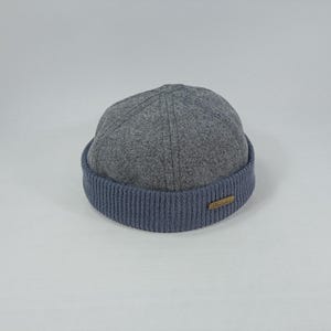 May include: A grey wool beanie with a blue ribbed cuff. The beanie has a small brown label on the cuff.