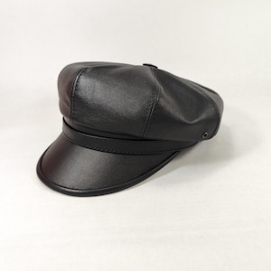May include: A black leather newsboy cap with a rounded crown and a short, stiff brim. The cap features a band around the crown and is set against a white background. The hat is a classic style.