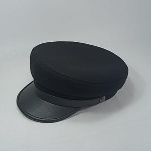 Peut inclure: Une casquette en laine noire avec une visière en cuir noir et un bouton noir sur le côté.