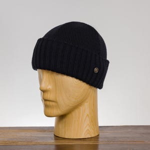 K&ouml;nnte beinhalten: Eine schwarze Strickm&uuml;tze mit einem kleinen goldenen Logo an der Seite.