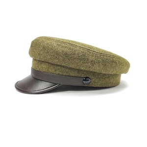 Op de afbeelding: Olijfgroene wollen hoed met een donkerbruin leren klep en band. De hoed heeft een afgeronde kroon en een kleine, zwarte knoop als detail aan de zijkant. Een klassieke hoed, geschikt voor diverse gelegenheden.