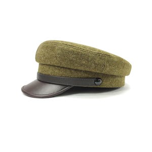Op de afbeelding: Olijfgroene wollen hoed met een donkerbruin leren vizier en band. De hoed heeft een klassiek, militair geïnspireerd ontwerp met een knoopdetail aan de zijkant. Een stijlvol accessoire.