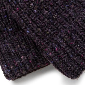 May include: Close-up of a dark purple knitted fabric with a ribbed texture. The fabric has flecks of blue, pink, and green throughout, adding visual interest. The material appears to be soft and warm, suitable for winter wear.