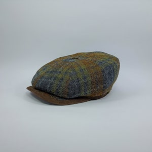 May include: A brown, green and grey tweed newsboy cap with a brown leather brim.