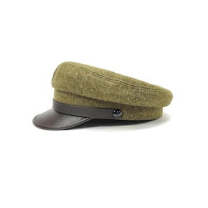 Op de afbeelding: Olijfgroene pet in militaire stijl met een donkerbruin leren vizier en band. De pet heeft een ronde kroon en een kleine, zwarte knoop. De hoed is gemaakt van een textuurstof.