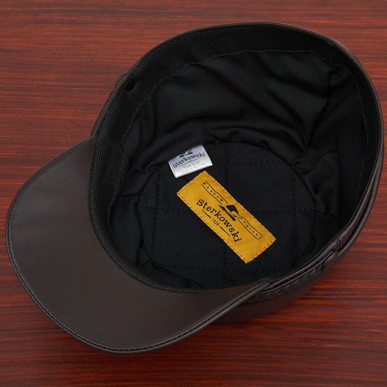 May include: A brown leather baseball cap with a black quilted lining. The cap has a label inside that reads "Sterkowski 1928 Made in Poland".
