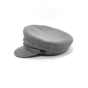 May include: A gray, flat-topped hat with a small, curved brim. The hat has a rounded crown and a band around the base. A black button is on the side. The hat is made of a soft, textured fabric.