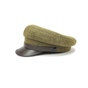 Op de afbeelding: Olijfgroene militaire pet met een donkerbruin leren klep en band. De pet heeft een afgeronde kroon en een kleine, zwarte knoop. De pet is gemaakt van een textuurstof en staat tegen een witte achtergrond.