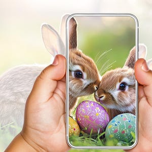 Puede incluir: Un teléfono inteligente que muestra una foto de dos conejos marrones con huevos de Pascua rosas y verdes. Los conejos se miran y los huevos están en la hierba.
