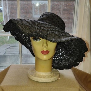 May include: A large black crochet sun hat with a wide brim. The hat is sitting on a mannequin head.