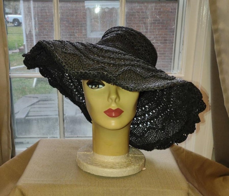 May include: A large black crochet sun hat with a wide brim. The hat is sitting on a mannequin head.
