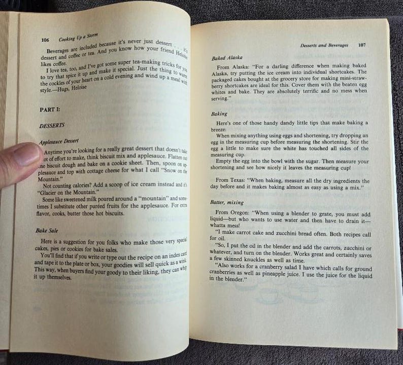May include: Open book with text about desserts and beverages, including recipes for applesauce dessert and baked Alaska. The pages are yellowed with age, suggesting a vintage cookbook.