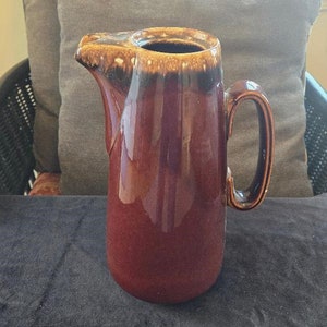 May include: A brown and cream glazed ceramic pitcher with a handle. The pitcher has a mottled glaze with brown and cream colors.