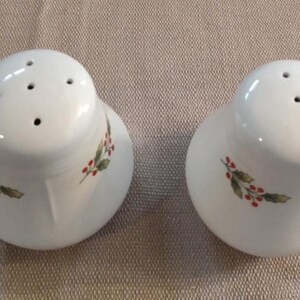 May include: Two white ceramic salt and pepper shakers with a holly and berry design. The shakers have four holes on the top for dispensing salt and pepper.