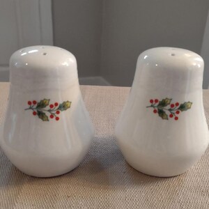 May include: A set of two white ceramic salt and pepper shakers with a green holly sprig and red berries design.