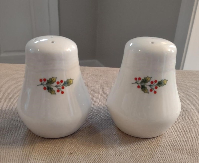 May include: A set of two white ceramic salt and pepper shakers with a green holly sprig and red berries design.