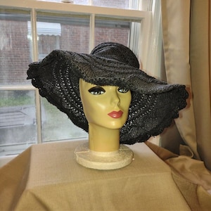 May include: A black crocheted sun hat with a wide brim and a large crown. The hat is displayed on a mannequin head.