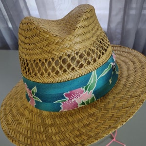 Peut inclure: Un chapeau de paille &agrave; large bord avec un bandeau floral bleu et rose. Le chapeau a un design tiss&eacute; et un ruban rose nou&eacute; autour de la couronne.