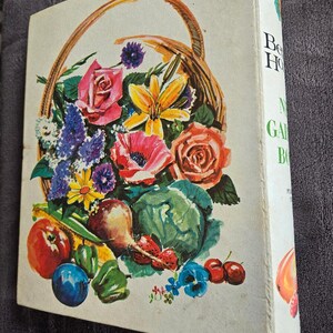May include: A vintage gardening book with a colorful illustration of a basket overflowing with flowers, fruits, and vegetables. The cover features roses, poppies, and a cabbage. The spine displays the title "Better Homes and Gardens".